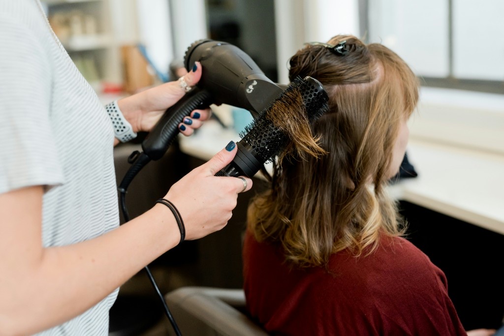 Hairstylist blow-drying a client while booking calls go unanswered